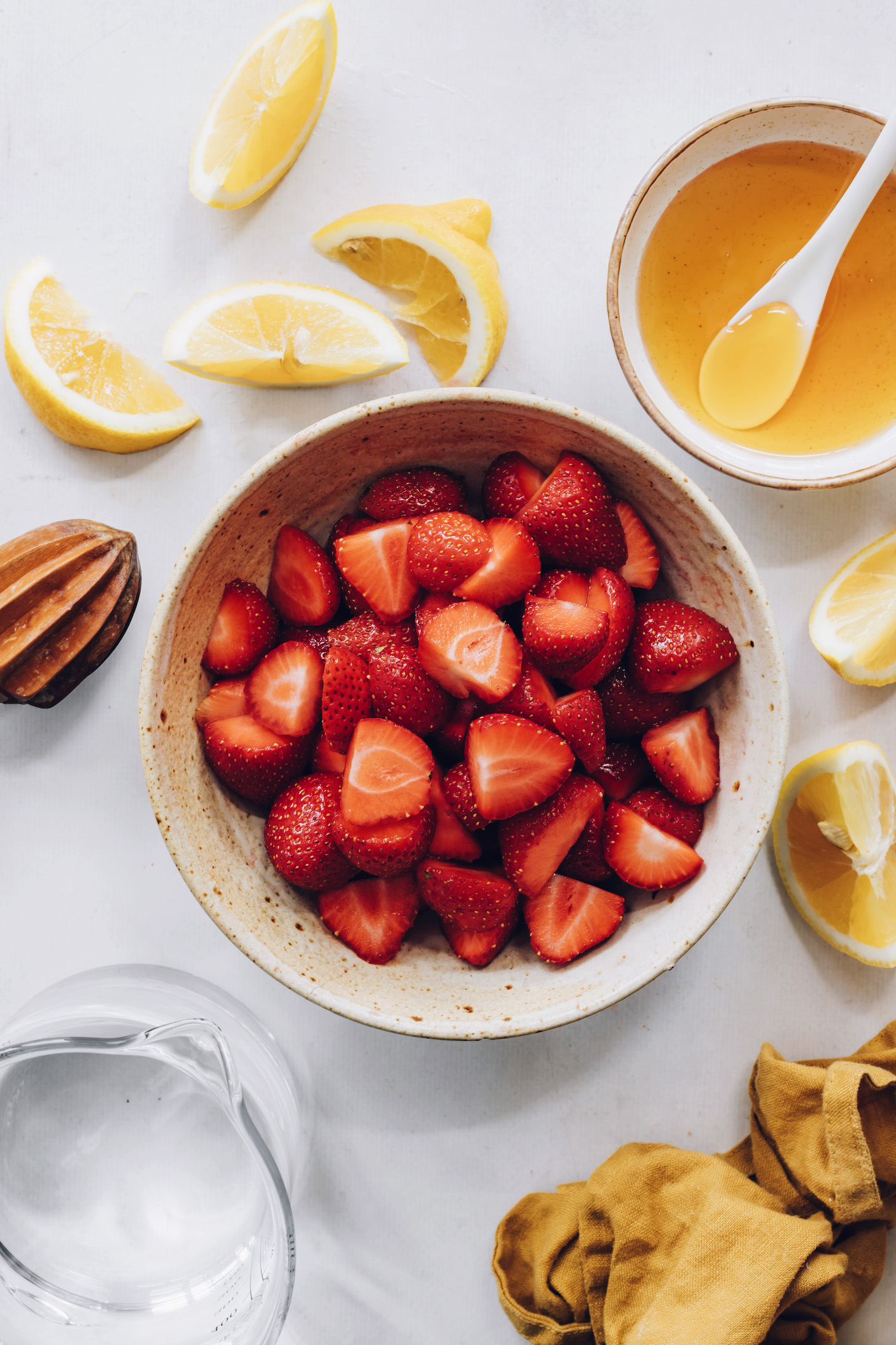 Lemon wedges, agave, and water around a bowl of sliced strawberries