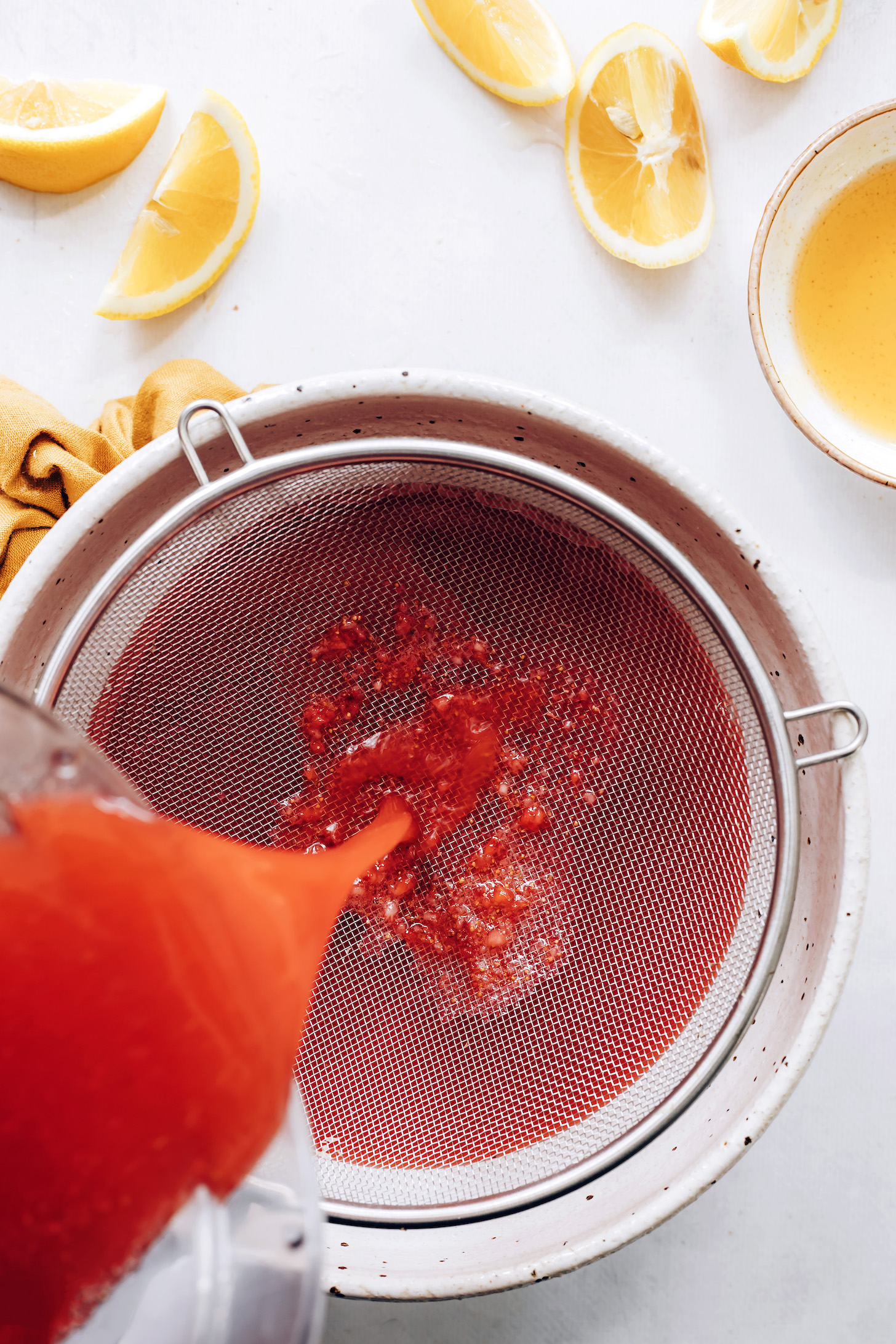 Pouring strawberry lemonade through a fine mesh strainer to remove strawberry seeds