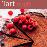Slices cut out of a whole vegan and gluten-free raspberry chocolate ganache tart with raspberries on top