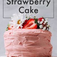Vegan and gluten-free strawberry cake on a cake plate with fresh strawberries and flowers on top