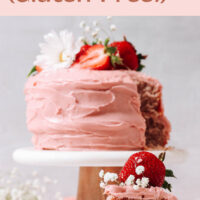 Slice of vegan and gluten-free strawberry cake with a whole strawberry cake, with fresh strawberries and flowers on top