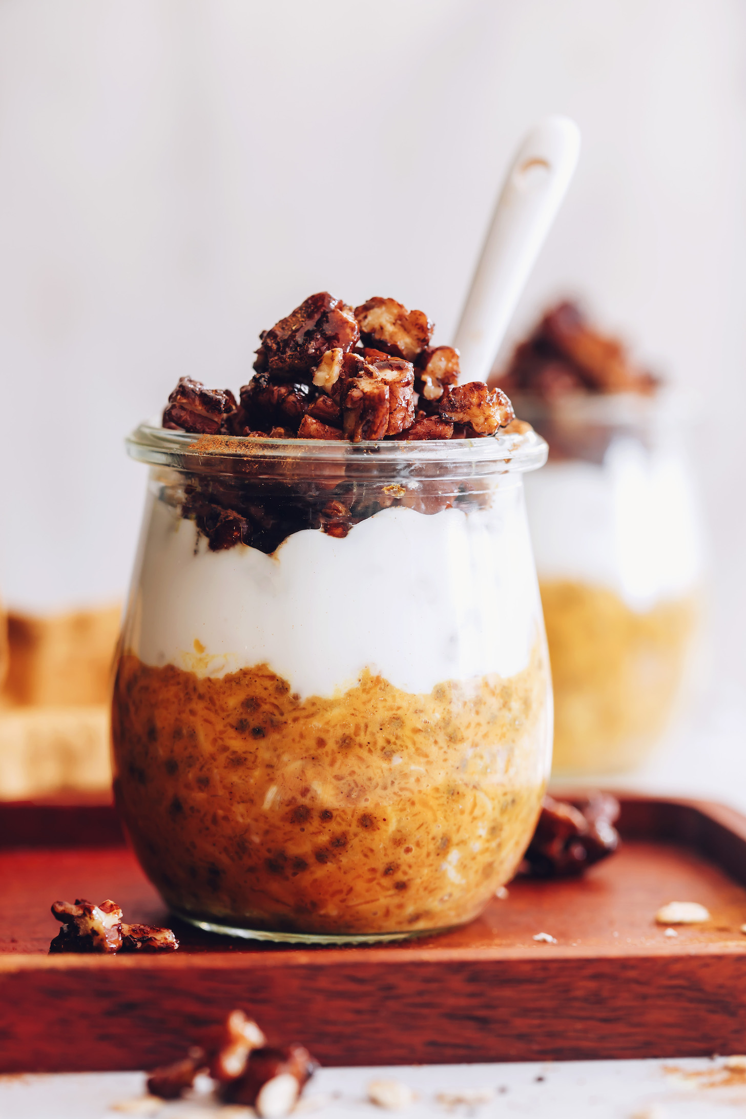 Close up shot of a jar of pumpkin overnight oats topped with coconut yogurt and candied pecans