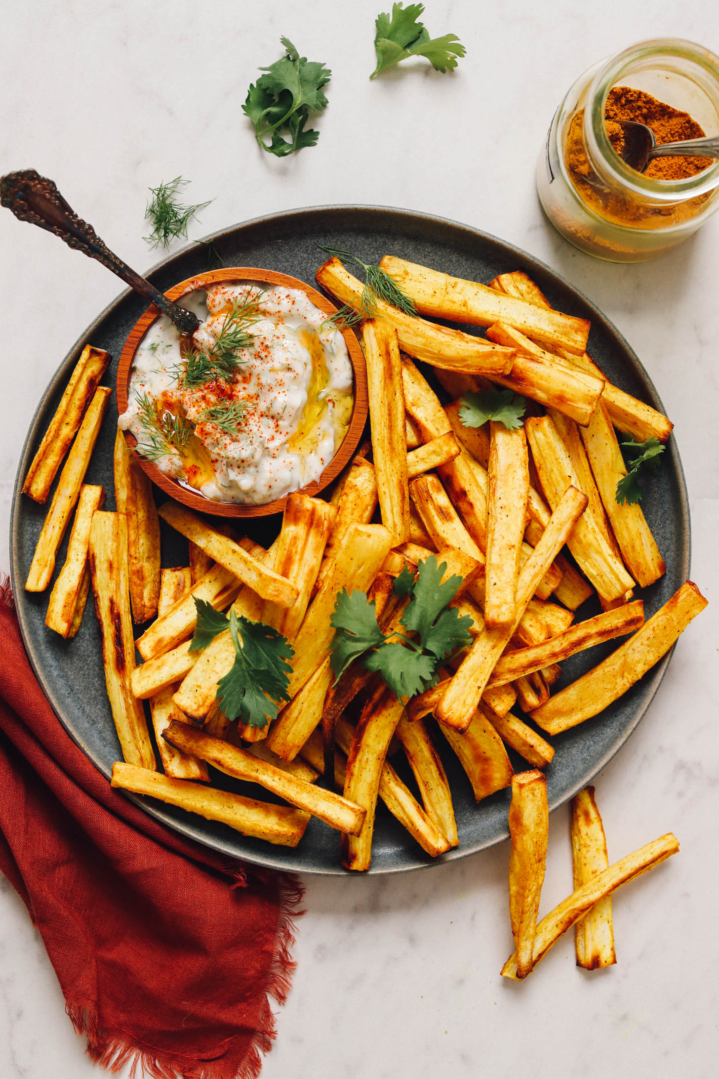 Curry powder next to a plate of baked parsnip fries and dairy-free yogurt sauce