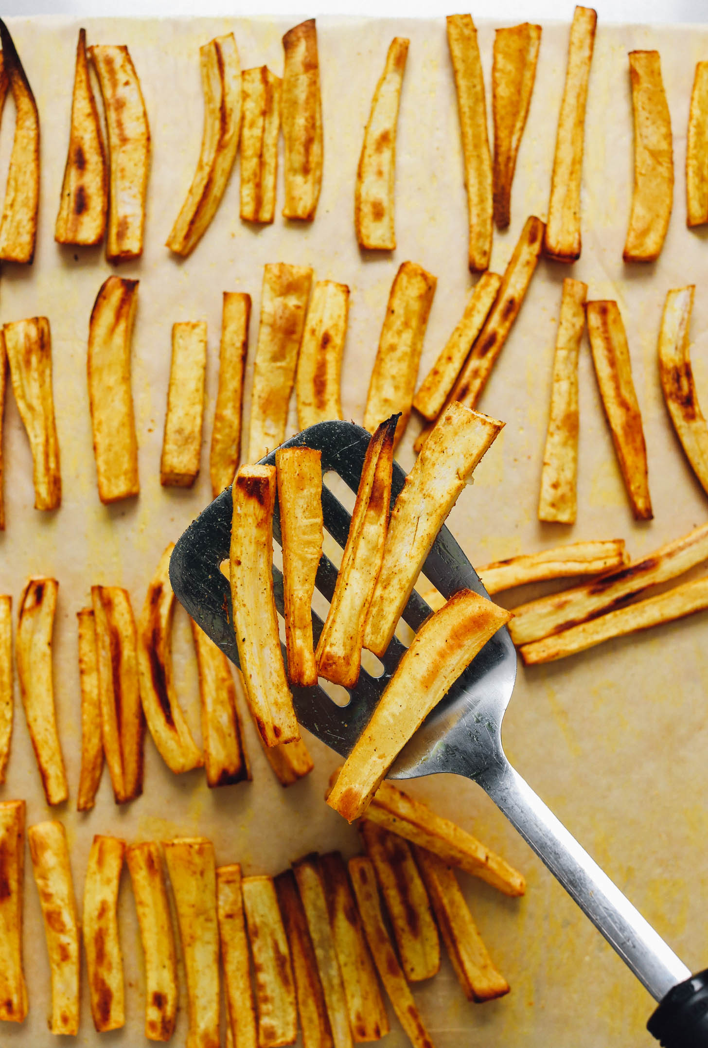 Perfectly browned parsnip fries on a baking sheet and spatula