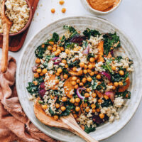 Wooden spoon in a bowl of hearty kale salad with chipotle pecan pesto