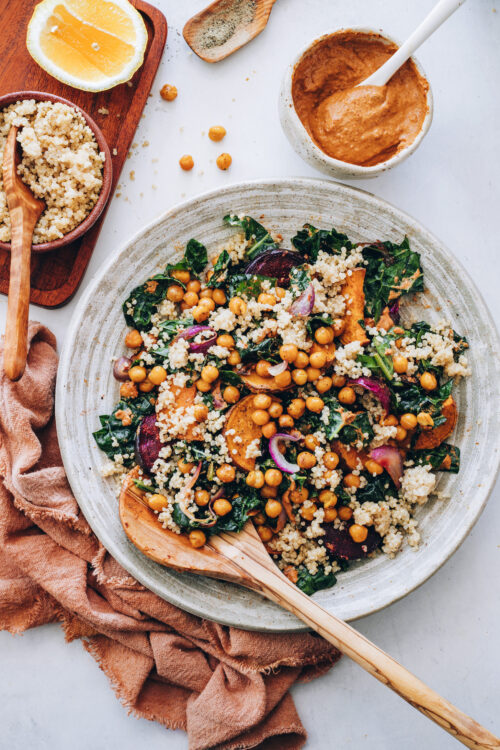 Wooden spoon in a bowl of hearty kale salad with chipotle pecan pesto