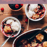 Baking dish and ramekins of vegan and gluten-free berry cobbler with vegan vanilla ice cream on top