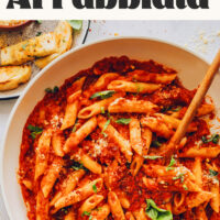 Pan of pasta with spicy red sauce with text above it saying Easy Penne Arrabbiata made with 8 pantry staples!
