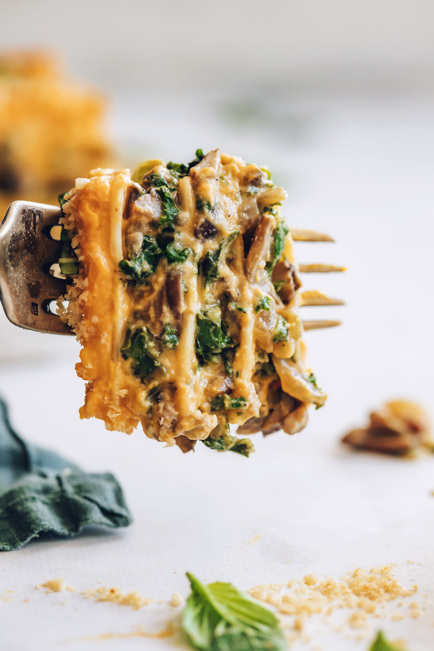 Fork holding up a bite of butternut squash, kale, and mushroom lasagna