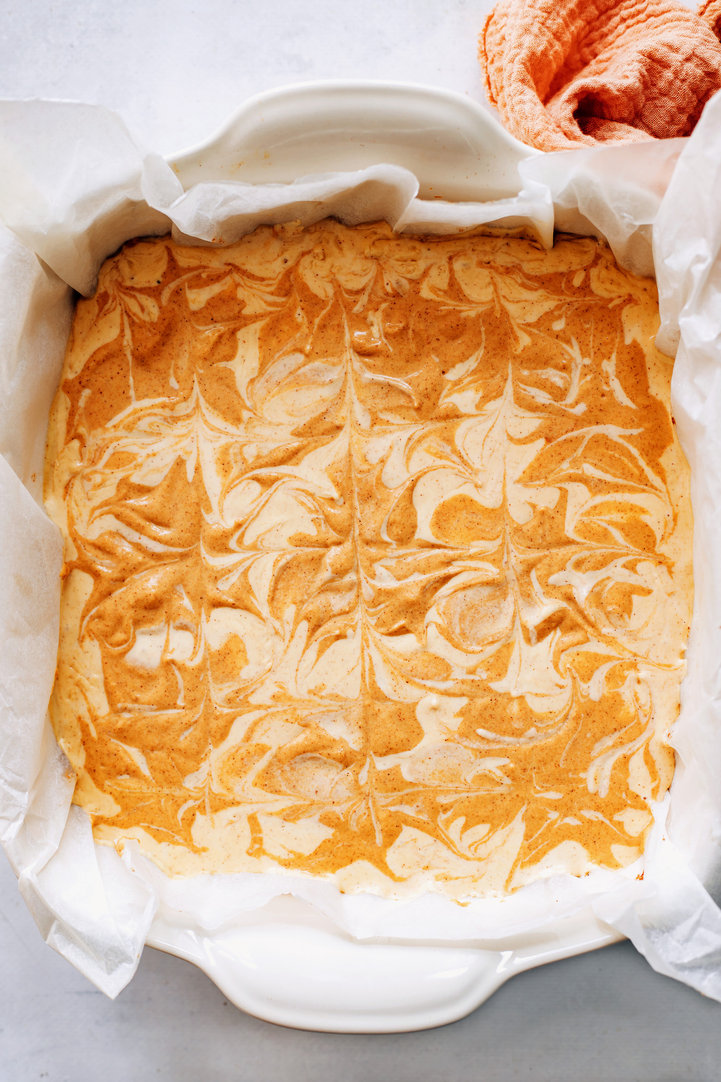 Parchment-lined baking dish showing pumpkin swirls in the cheesecake filling