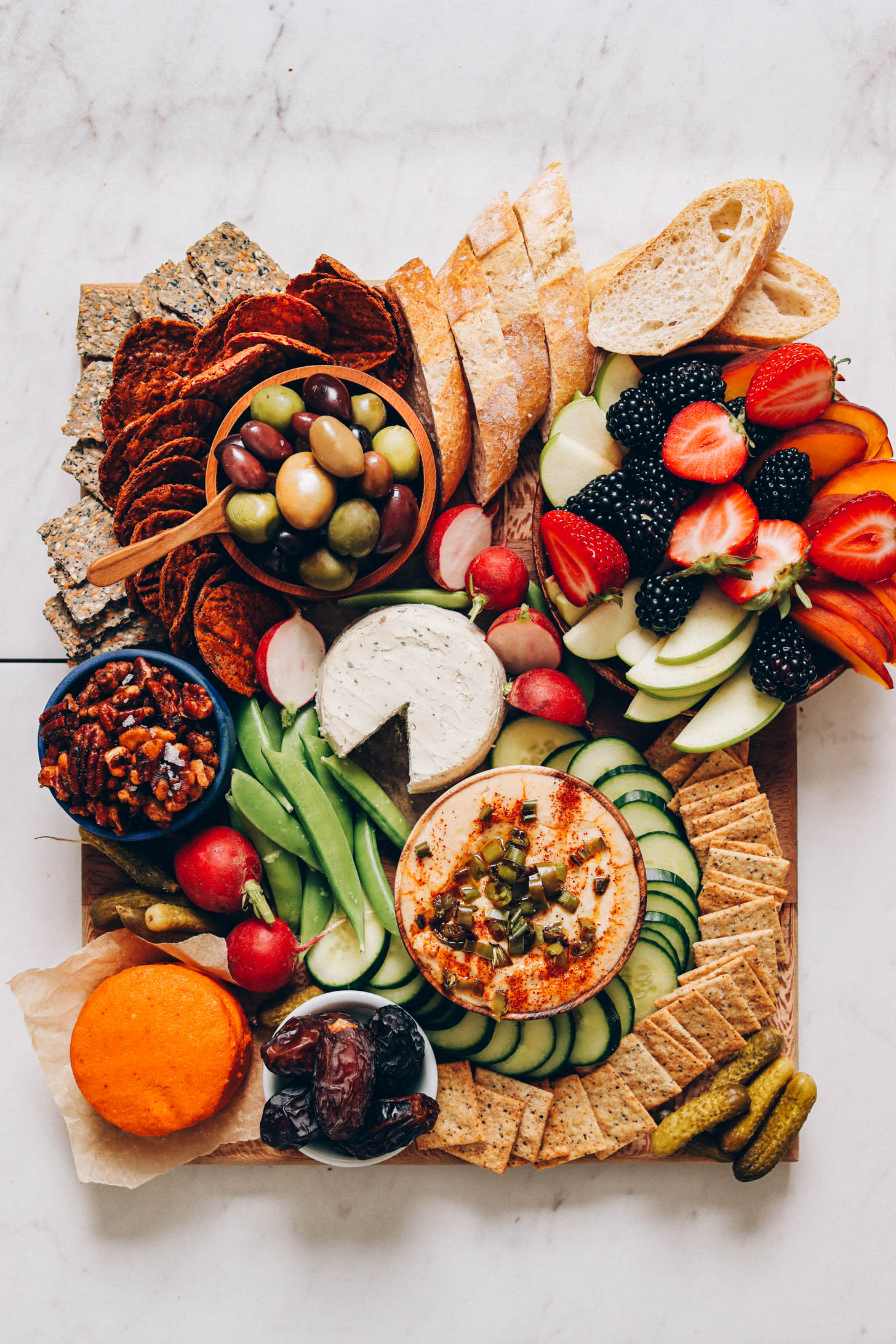 Abundant vegan charcuterie platter with fruit, nuts, crackers, veggies, dips, and more