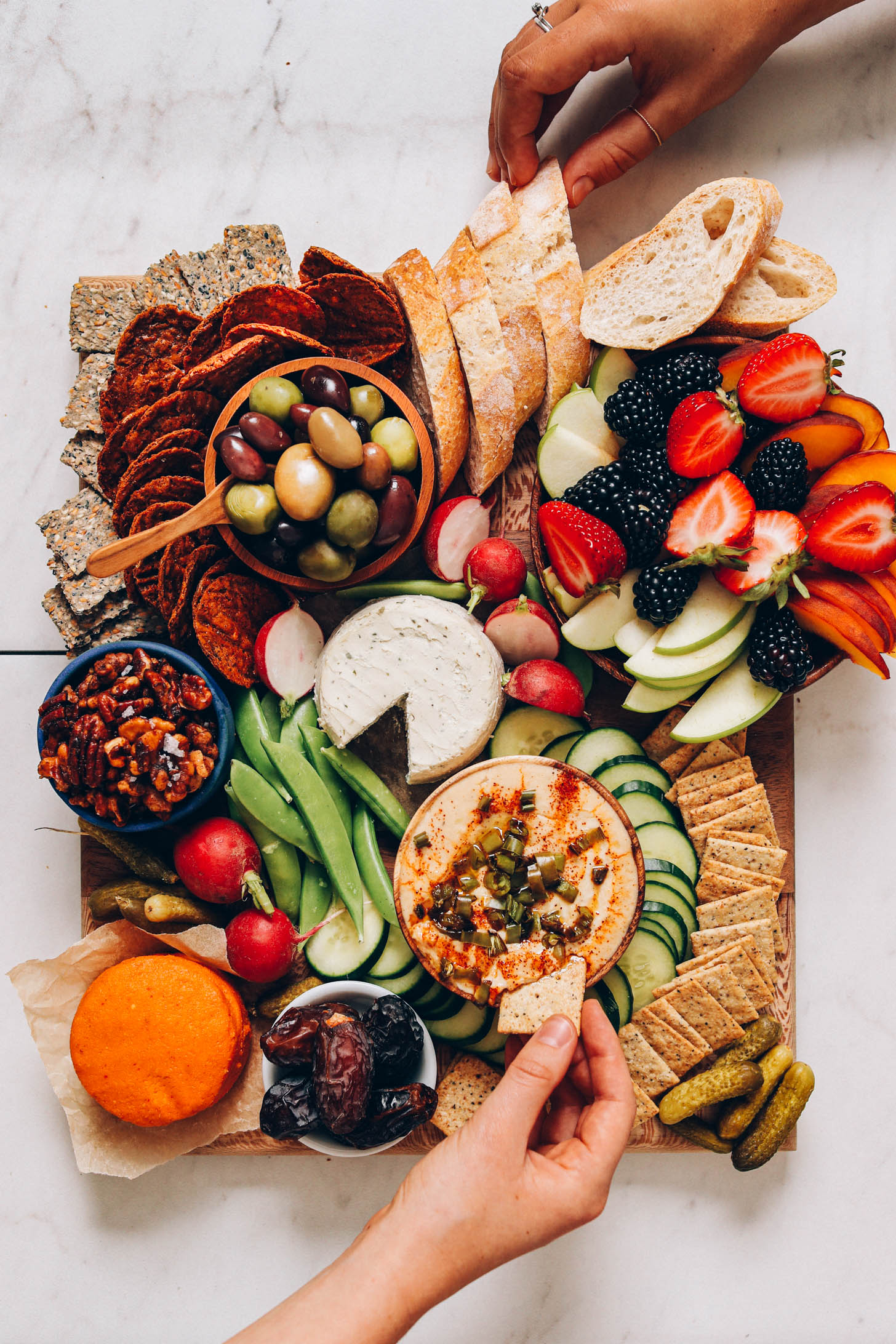 Hands reaching to grab snacks from a vegan charcuterie board