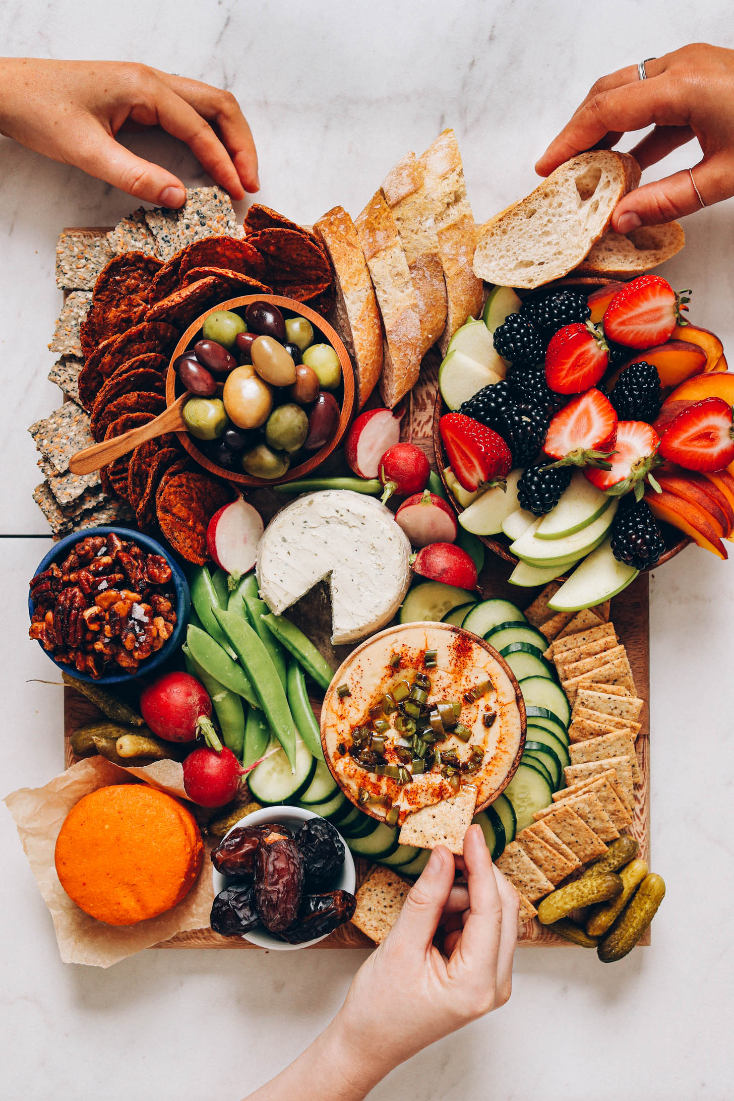 Hands grabbing snacks from a vegan charcuterie board