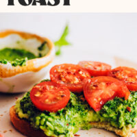 Slice of avocado toast topped with pesto and sliced cherry tomatoes