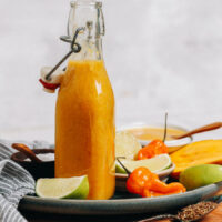 Bottle of mango habanero hot sauce next to limes, habaneros, and mango
