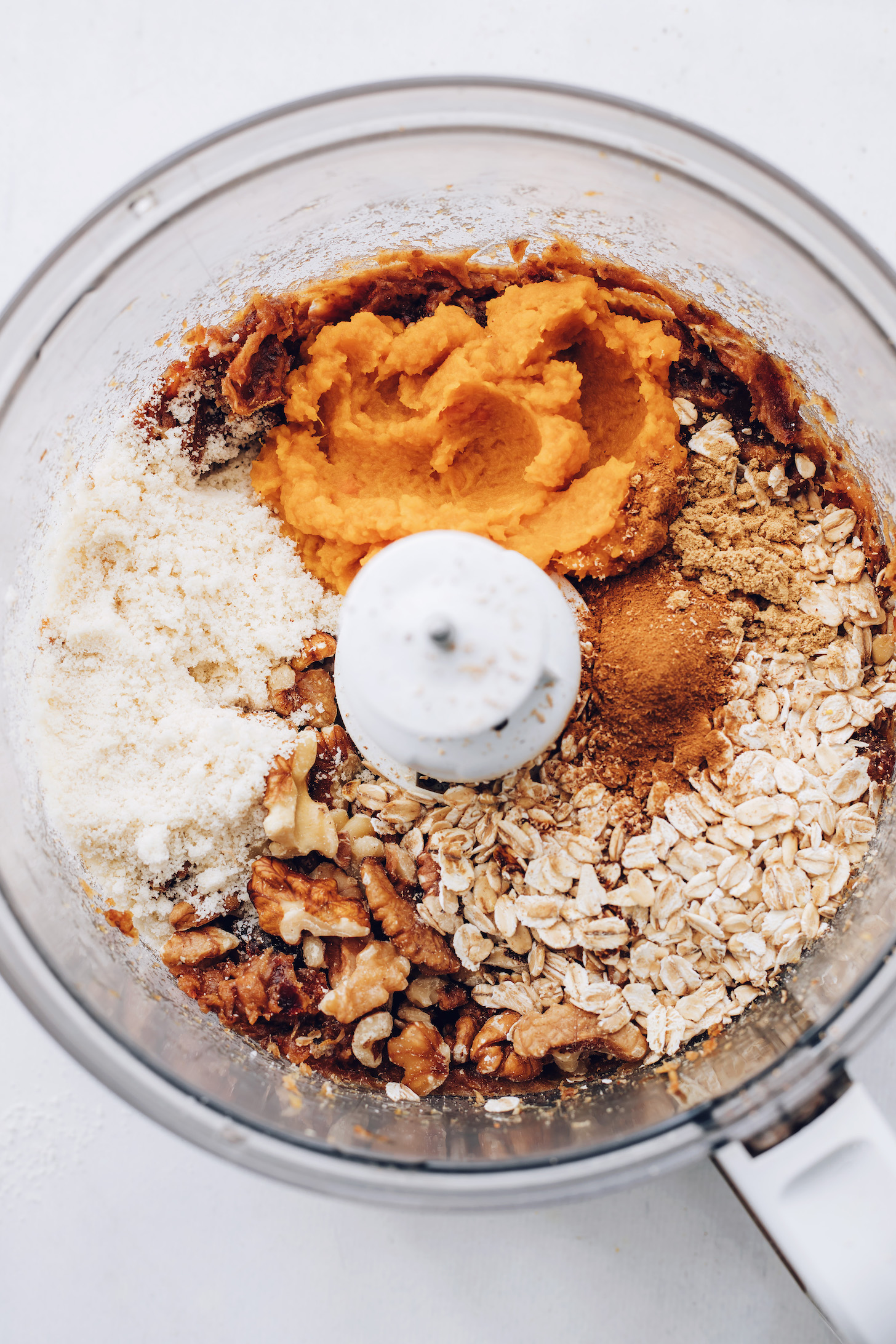 Food processor with date paste, almond flour, walnuts, oats, spices, and pumpkin purée