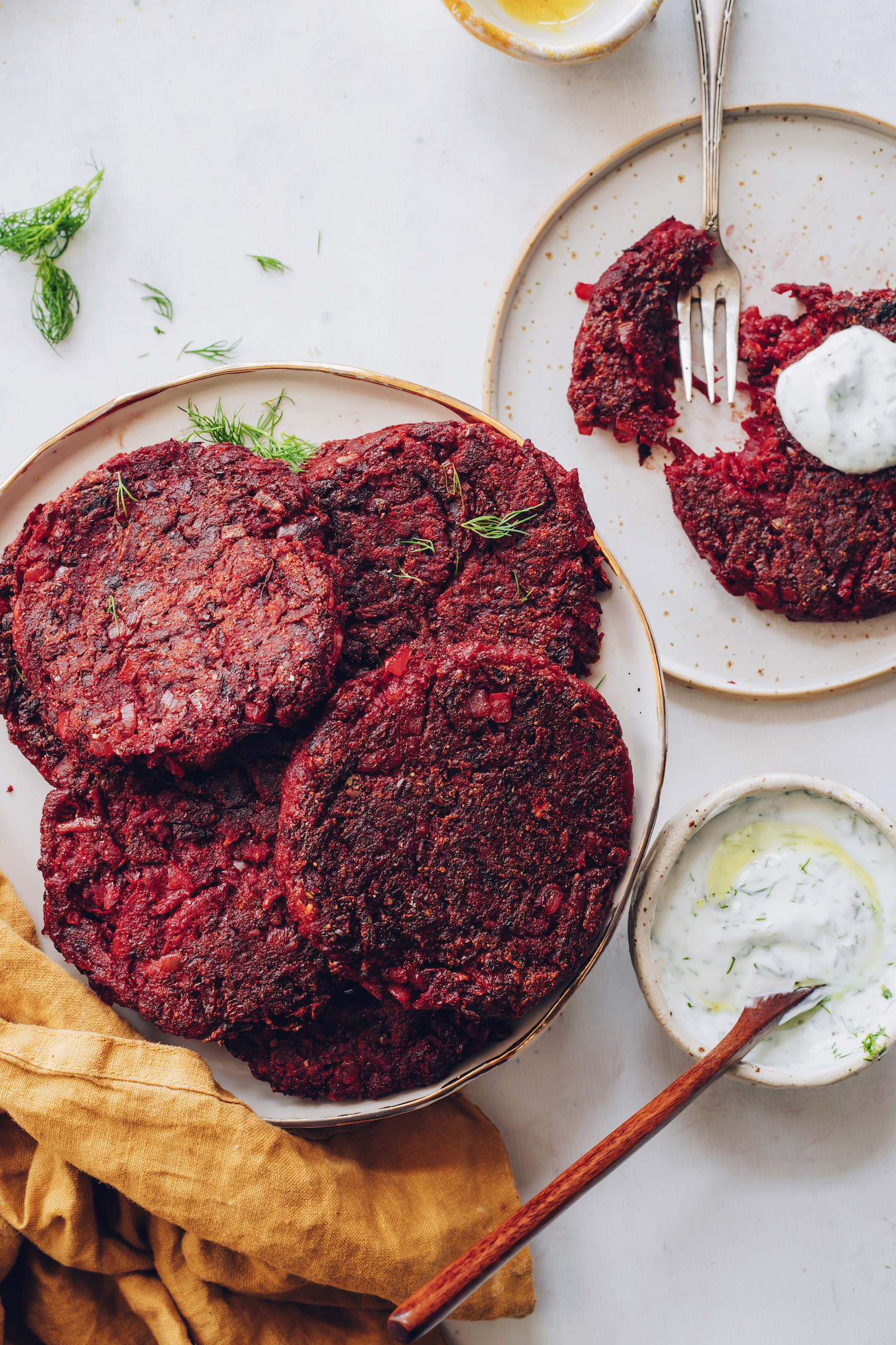 Plates of beet fritters with dill yogurt sauce on top and in a bowl on the side