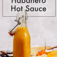 Jar of zesty mango habanero hot sauce with lime wedges and habanero peppers beside it