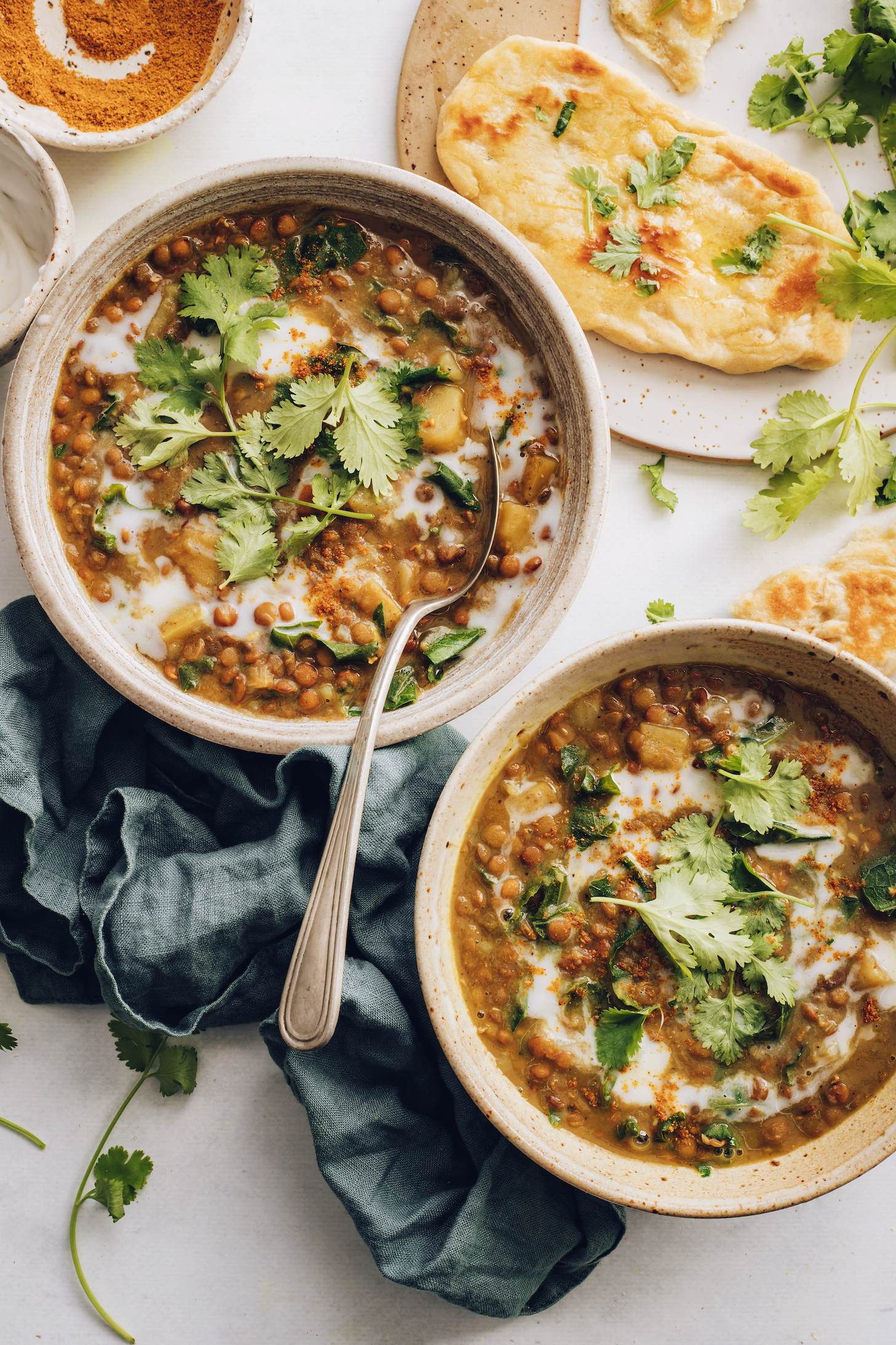 Curry powder and vegan naan next to bowls of Instant Pot lentil soup