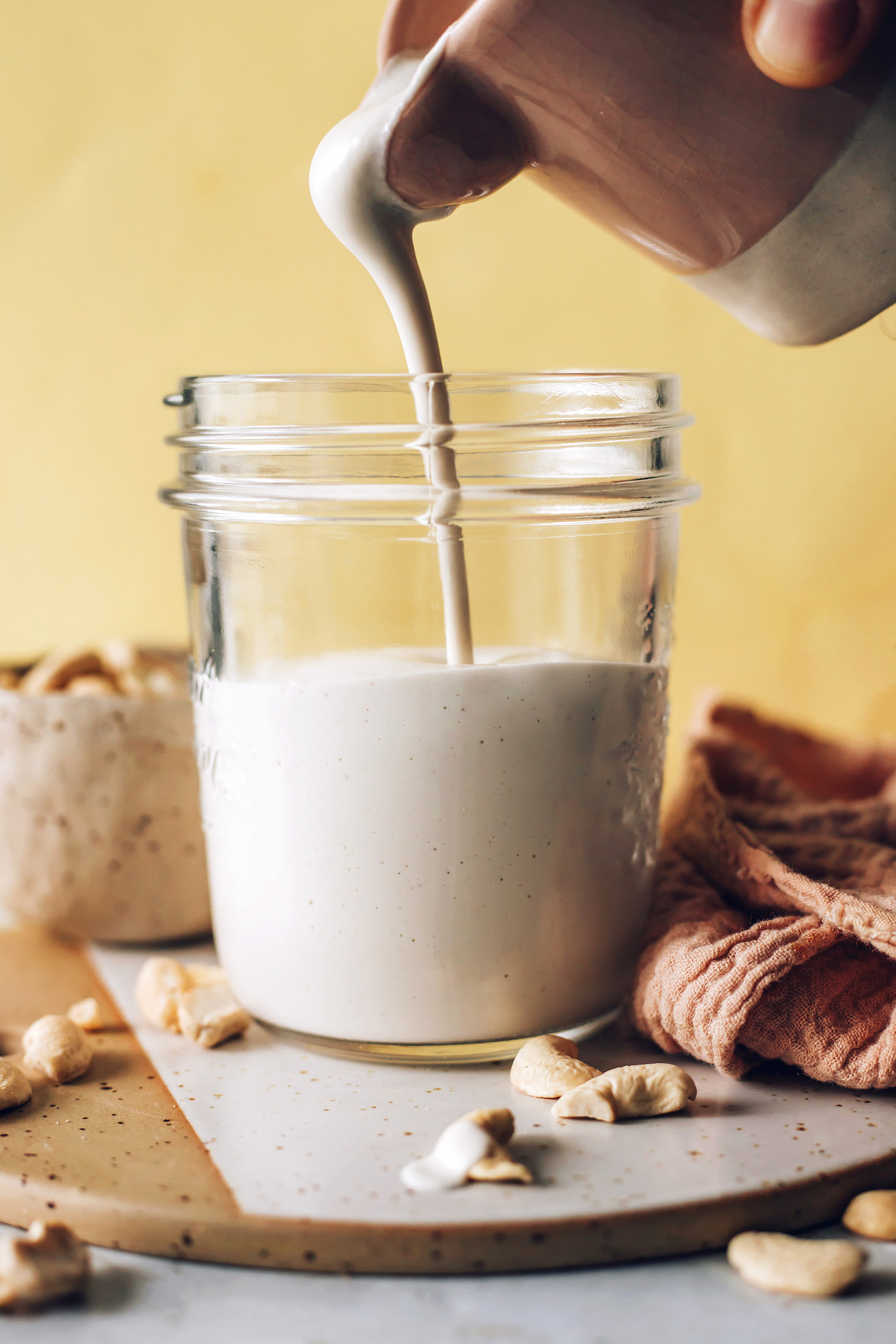 Pouring cashew cream from a mini pitcher into a glass jar