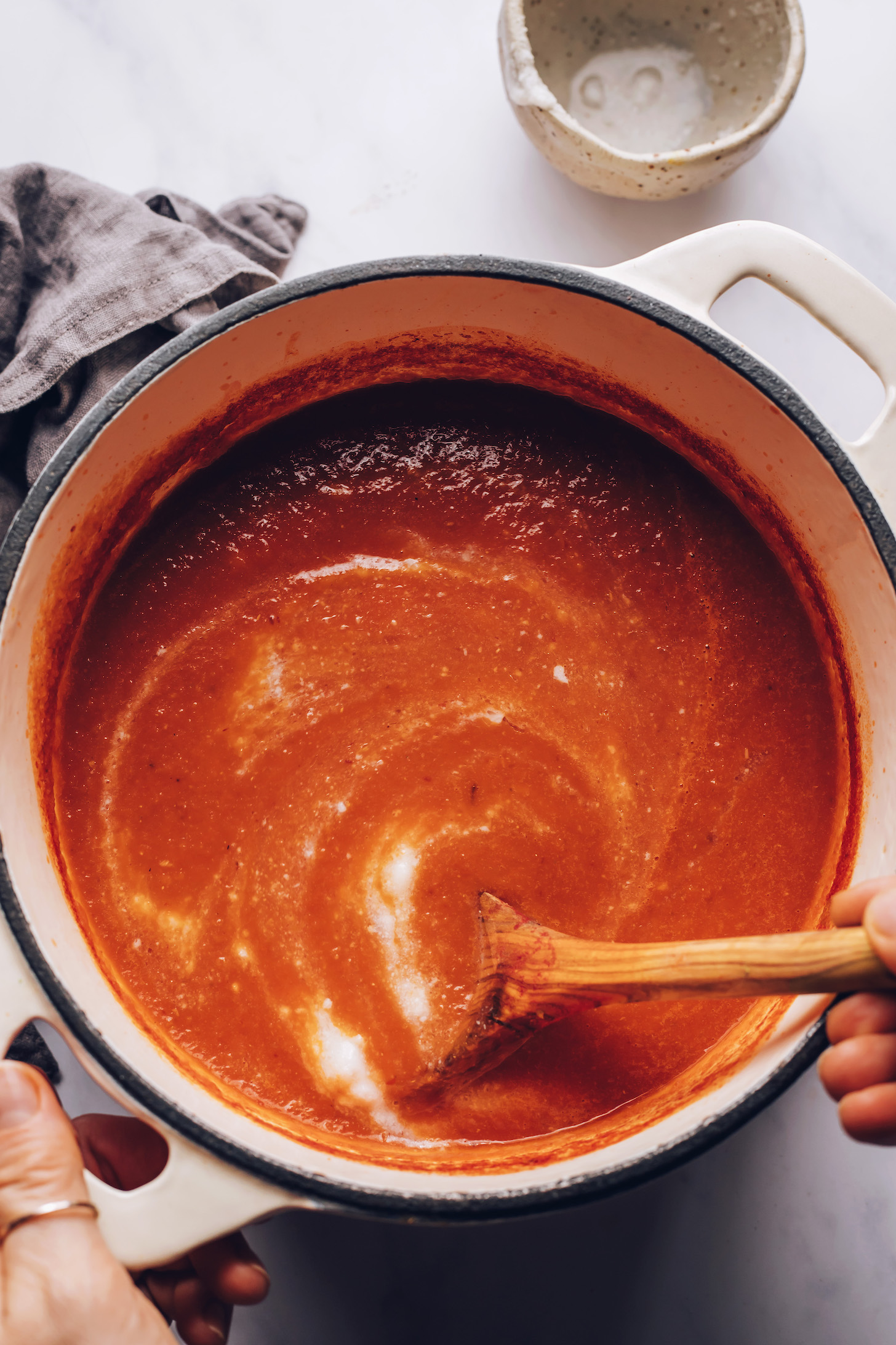 Using a wooden spoon to stir coconut milk into tomato soup in a Dutch oven