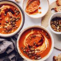 Bowls of spicy tomato soup topped with coconut milk and pepitas