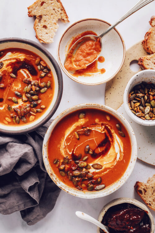 Bowls of spicy tomato soup topped with coconut milk and pepitas