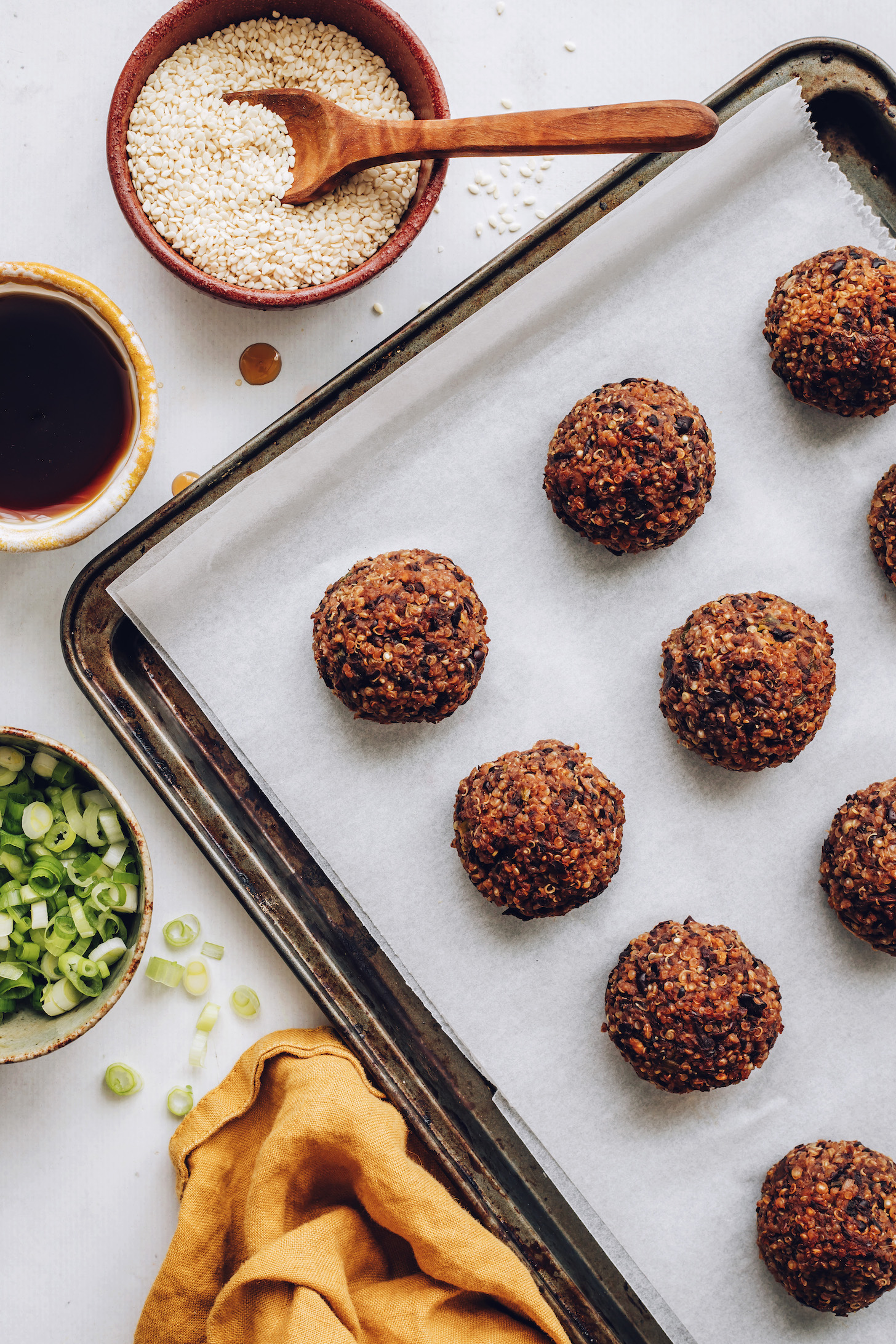 Bowls of green onions, tamari, and sesame seeds beside a baking sheet of ginger sesame vegan meatballs