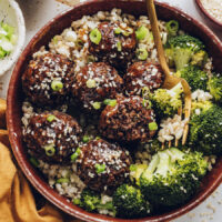 Fork in a bowl of rice, broccoli, and ginger sesame vegan meatballs