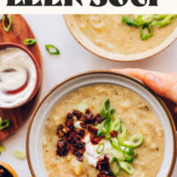 Holding the sides of a bowl of creamy vegan potato leek soup that says comforting and 1 pot above it