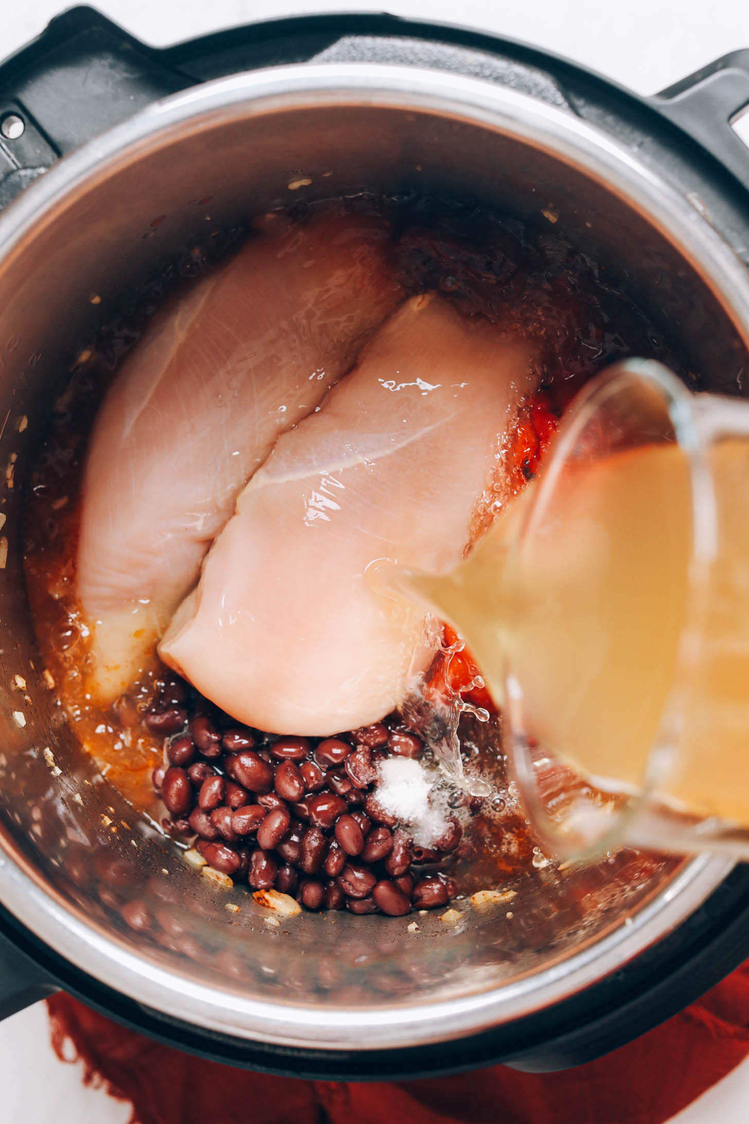 Pouring chicken broth over boneless skinless chicken breasts