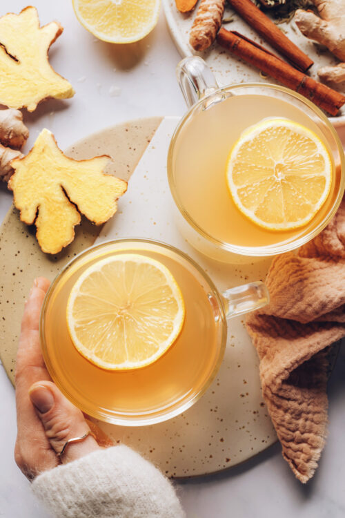 Holding a mug of fresh ginger tea topped with lemon slices