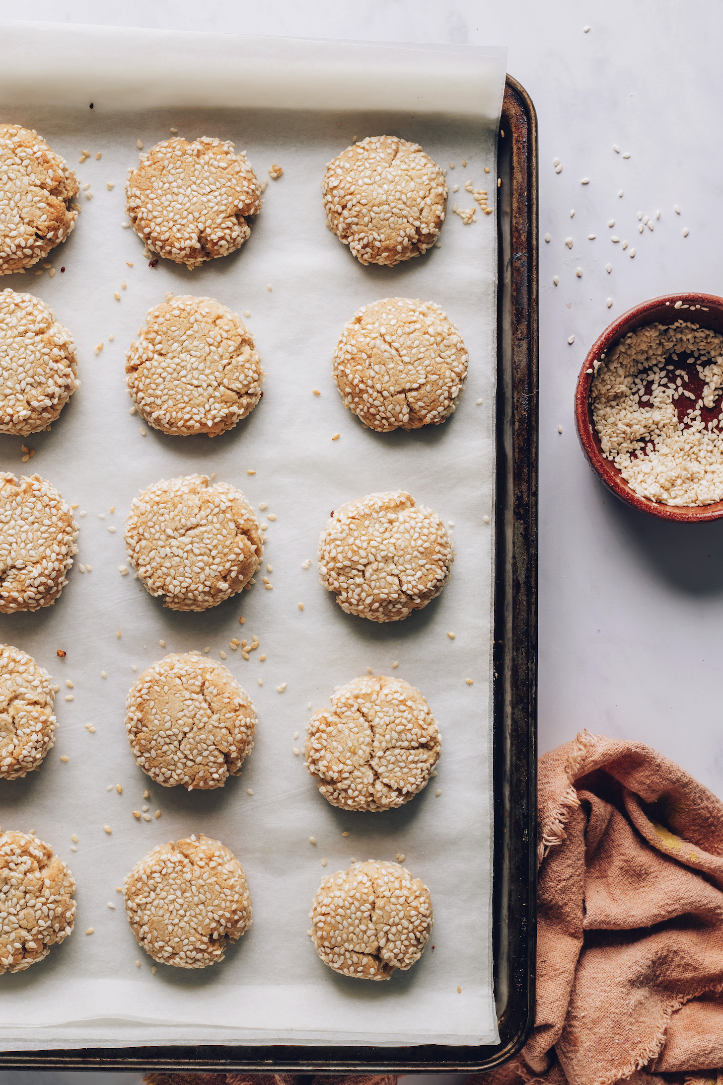 Baking sheet with baked tahini cookies coated in sesame seeds