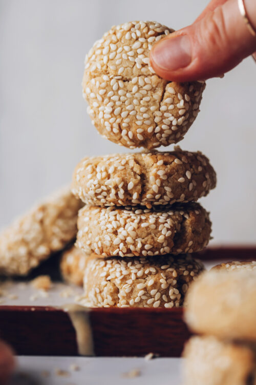 Picking up a tahini cookie from a stack on a plate