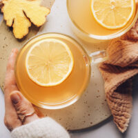 Hand holding a mug of fresh ginger tea with lemon
