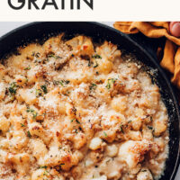 Skillet of vegan and gluten-free creamy cauliflower gratin with a wooden spoon in it