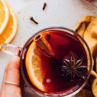 Hand holding a glass of tart cherry mulled "wine" with an orange slice, clove star, and cinnamon stick in it