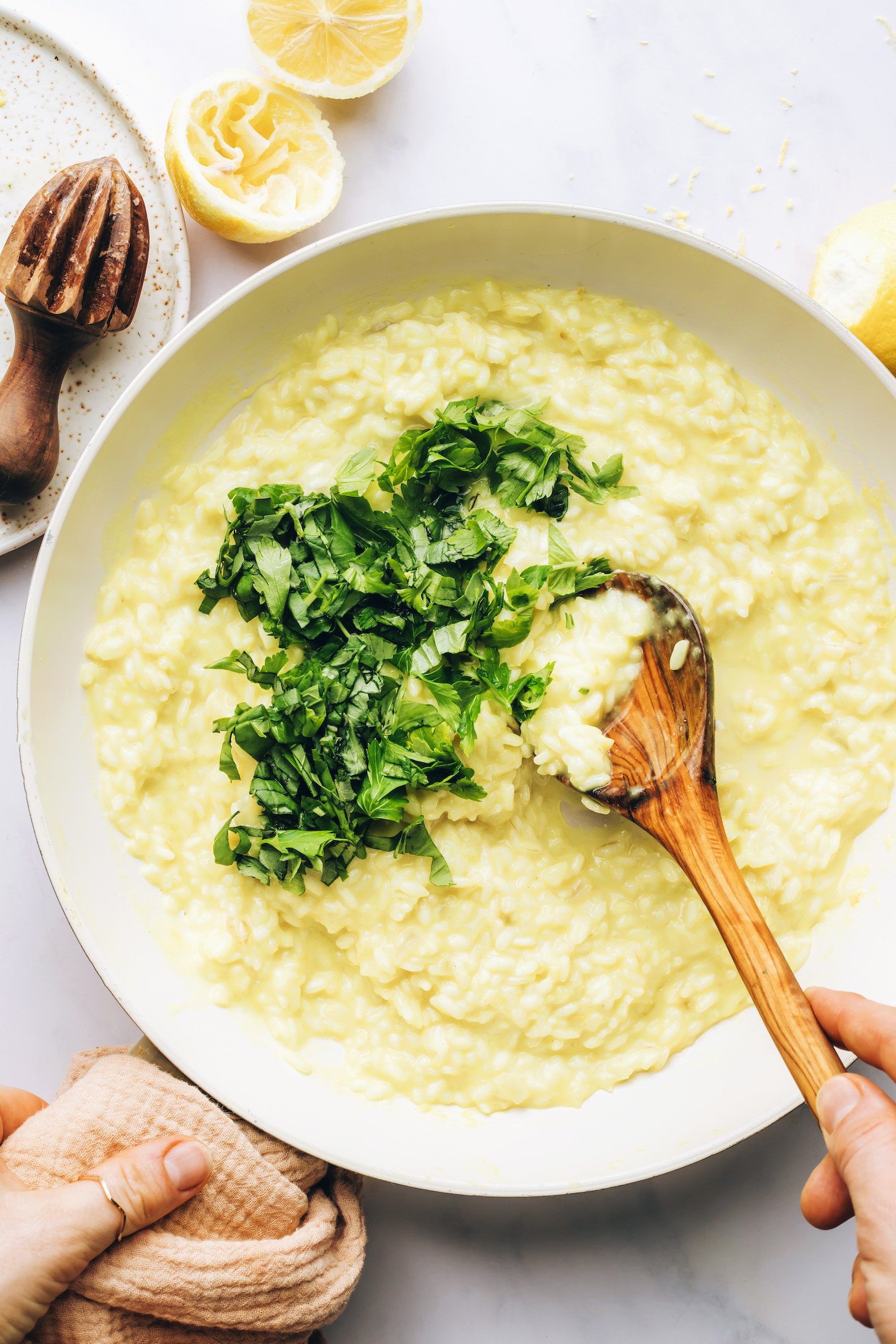 Hands stirring fresh parsley and basil into a creamy lemon risotto