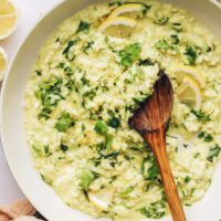 A wooden serving spoon in a large skillet of lemon and herb risotto