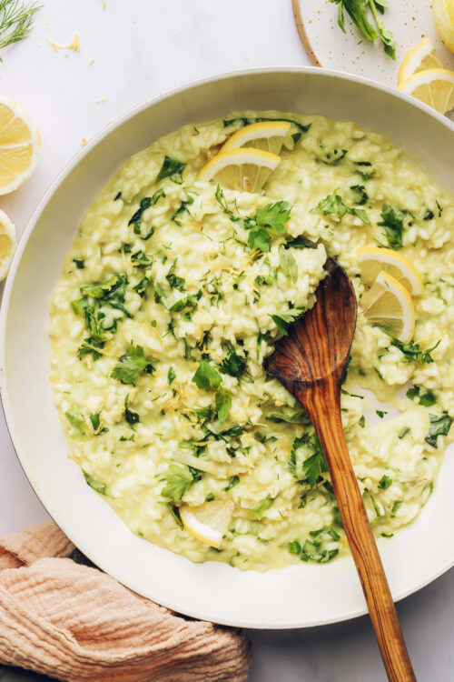 A wooden serving spoon in a large skillet of lemon and herb risotto