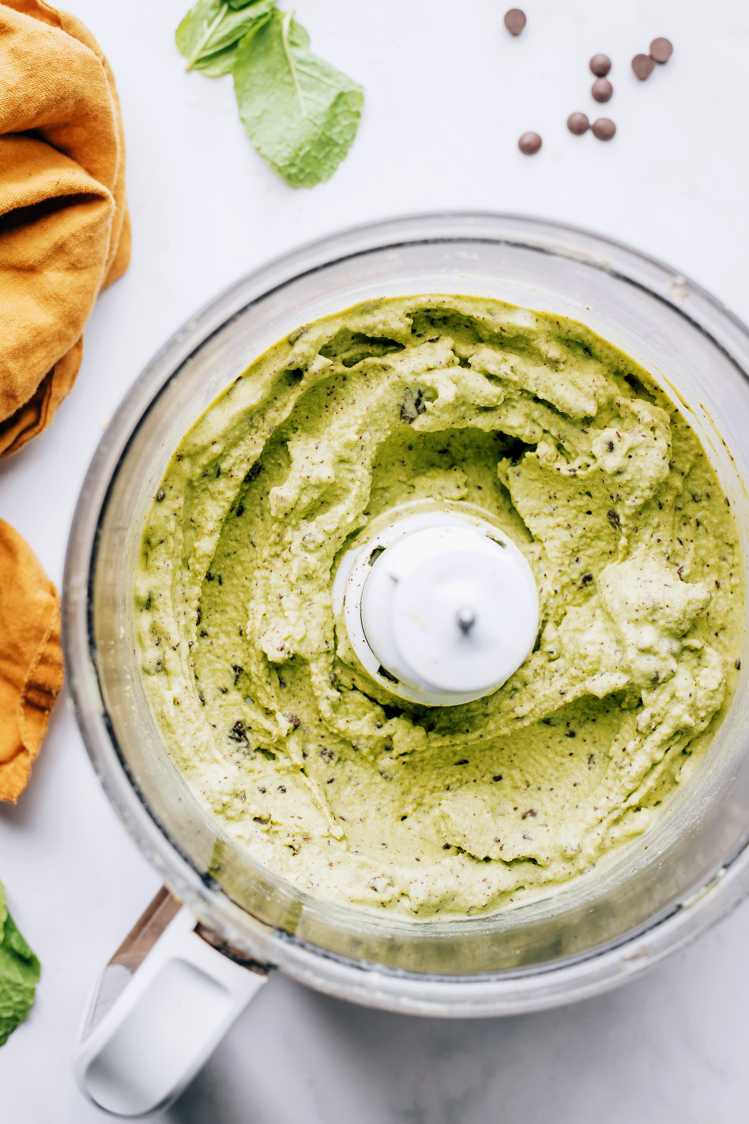 Food processor with creamy dairy-free mint chocolate chip soft serve in it