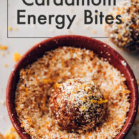 A vegan, gluten-free, no-bake orange cardamom energy bite being rolled in toasted coconut