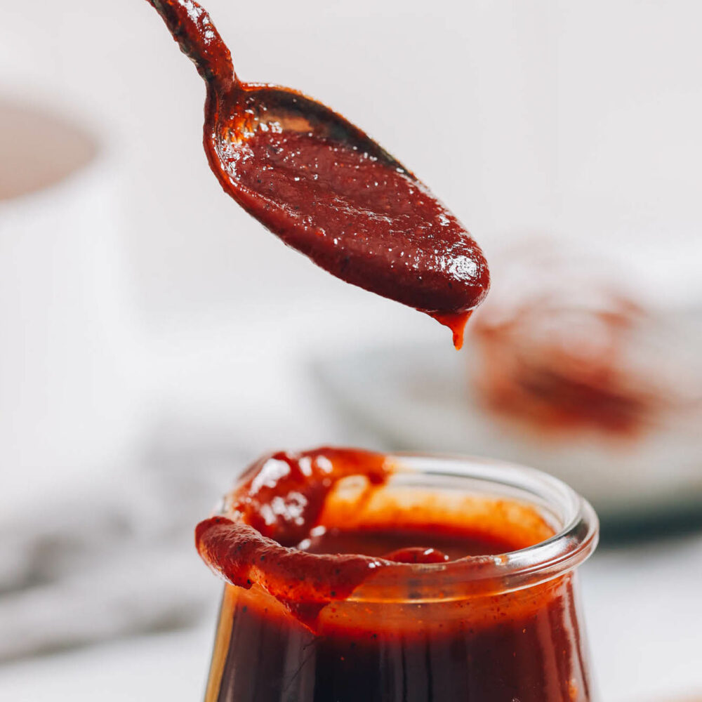 Close up shot of vegan gluten-free BBQ sauce in a spoon on top of a jar