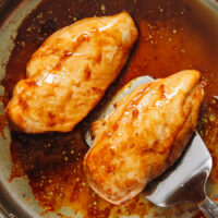 Holding a pan seared baked chicken breasts over a skillet