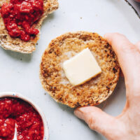 Hand picking up a gluten-free English muffin spread with vegan butter