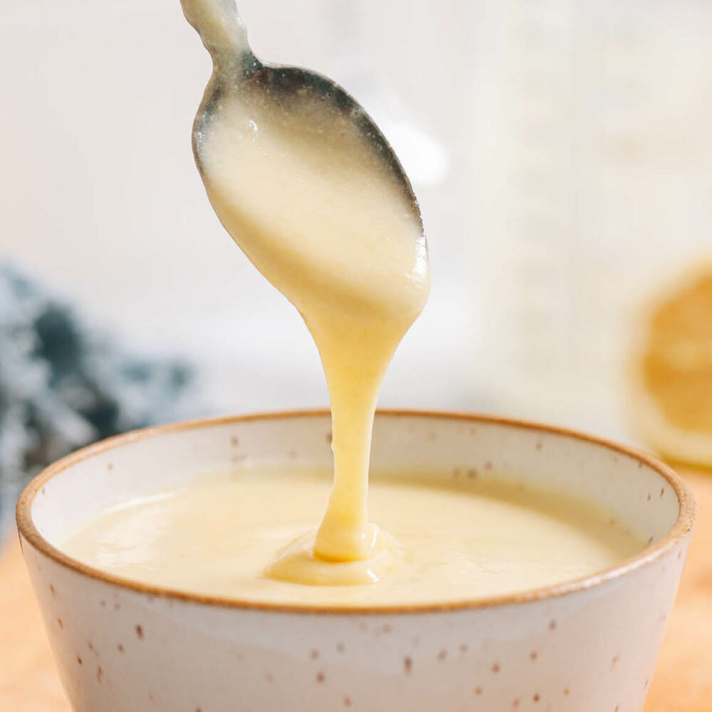 Vegan hollandaise sauce dripping from a spoon into a bowl