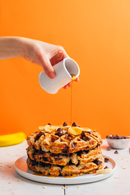 Pouring maple syrup over a stack of gluten-free waffles