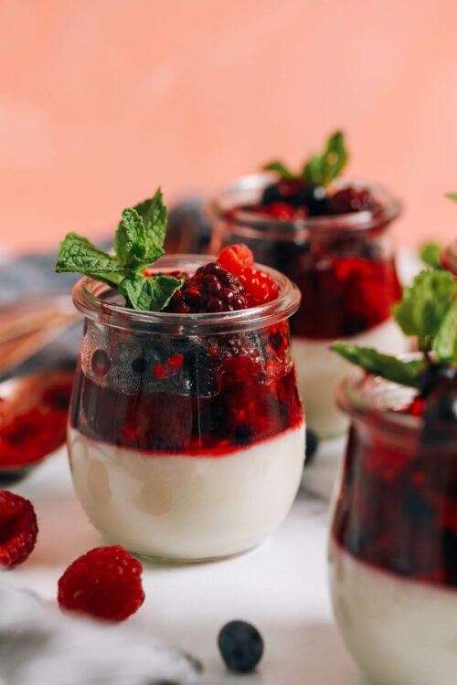 Jars of vegan panna cotta topped with a mixed berry compote