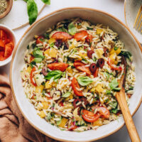 Wooden spoon in a bowl of our vegan orzo pasta salad