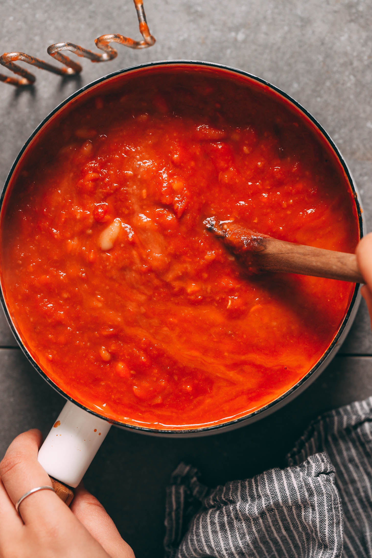Using a wooden spoon to stir white bean tomato soup
